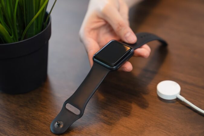 Une main tenant une montre connectée noire, avec un chargeur sans fil à côté, similaire à certaines montres caméras espions