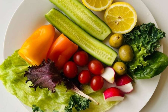 Une assiette blanche garnie de légumes frais et colorés pour manger sainement : concombre, poivron, tomates cerises, radis, olives et citron.