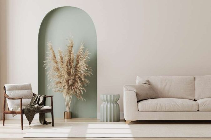 Un salon épuré inspiré de la décoration intérieure naturelle avec une arche verte sauge, des herbes de pampa et un canapé beige.