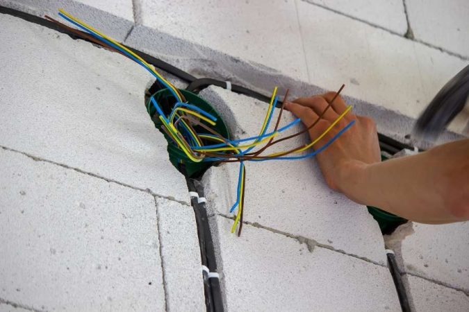 Un artisan installe des fils colorés dans une saignée murale pour apprendre à cacher les câbles électriques.