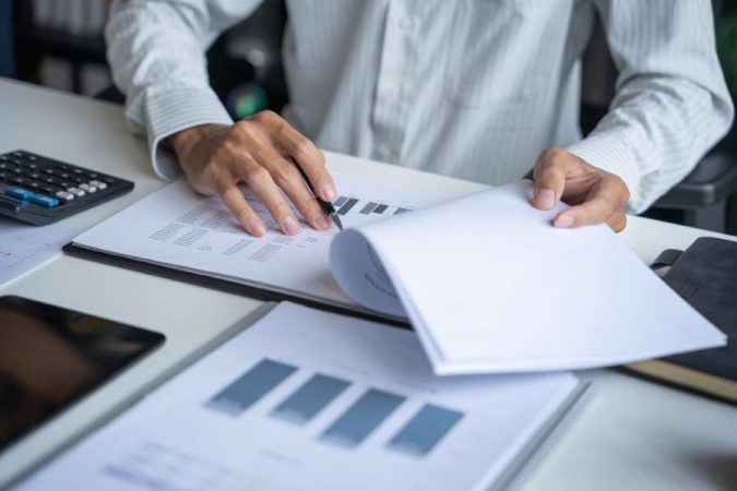 Un analyste en chemise examine des documents comptables et des graphiques financiers sur son bureau.