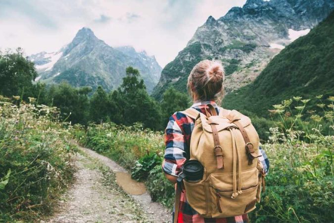 Une randonneuse avec un sac à dos en toile marche sur un sentier de montagne, observant un paysage naturel préservé, symbole d'un tourisme soucieux de son impact écologique.