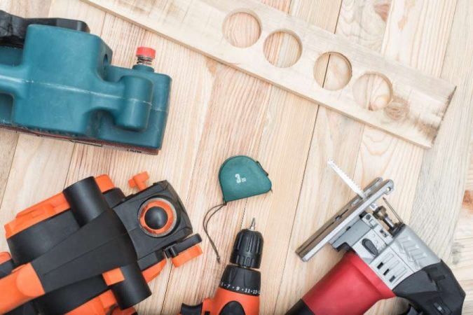 Plusieurs outils de menuiserie électroportatifs, comprenant une ponceuse, une perceuse et une scie sauteuse, sont disposés sur un établi en bois.